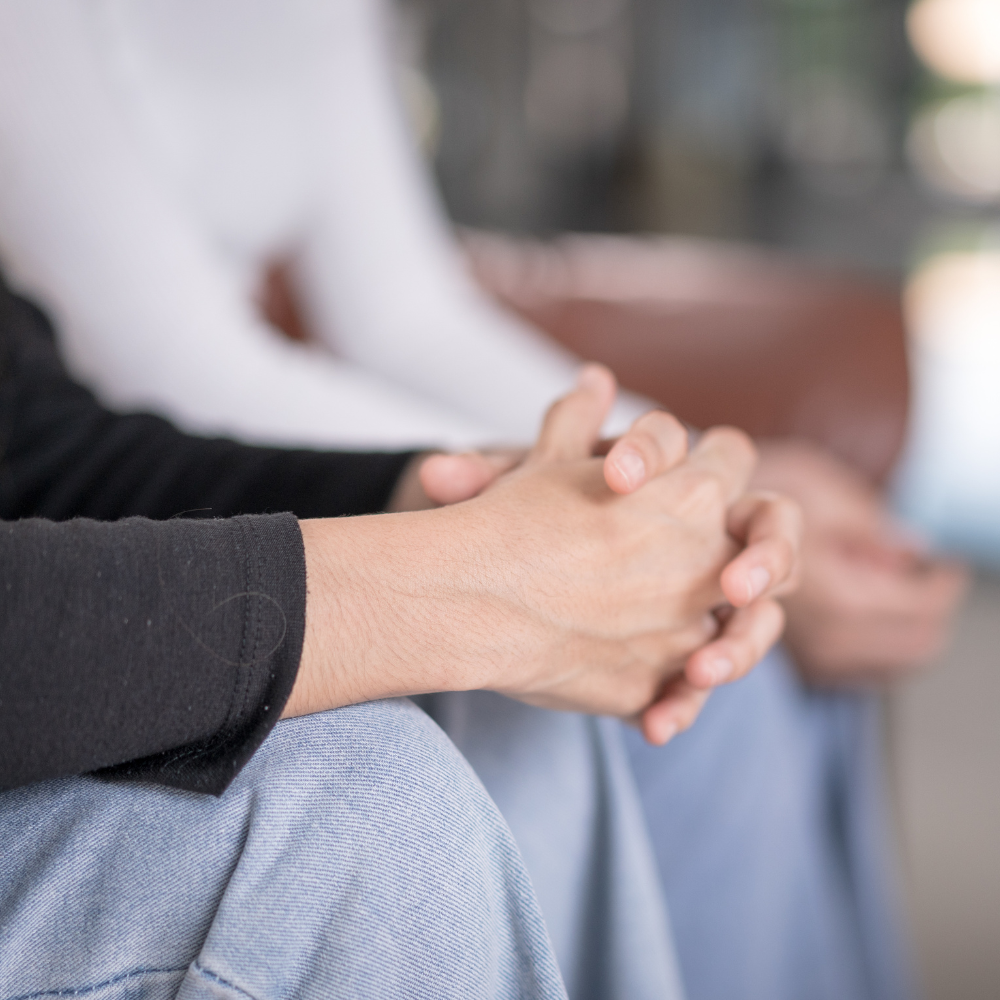 2 people sitting and talking with focus on hands crossed together